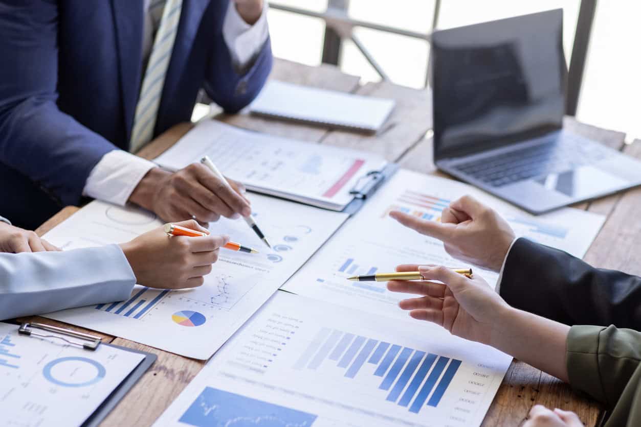 Group of confident business people point to graphs and charts to analyze market data, balance sheet, account, net profit to plan new sales strategies to increase production capacity.